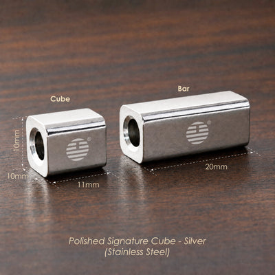 Two silver stainless steel polished signature cubes on a dark wood background, showing dimensions 10mm x 11mm for the smaller cube and 20mm x 10mm for the larger cube, with text reading 'Polished Signature Cube - Silver (Stainless Steel)'.