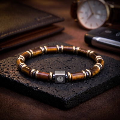 Bracelet with wooden beads on a dark stone surface, with a watch and phone in the background.