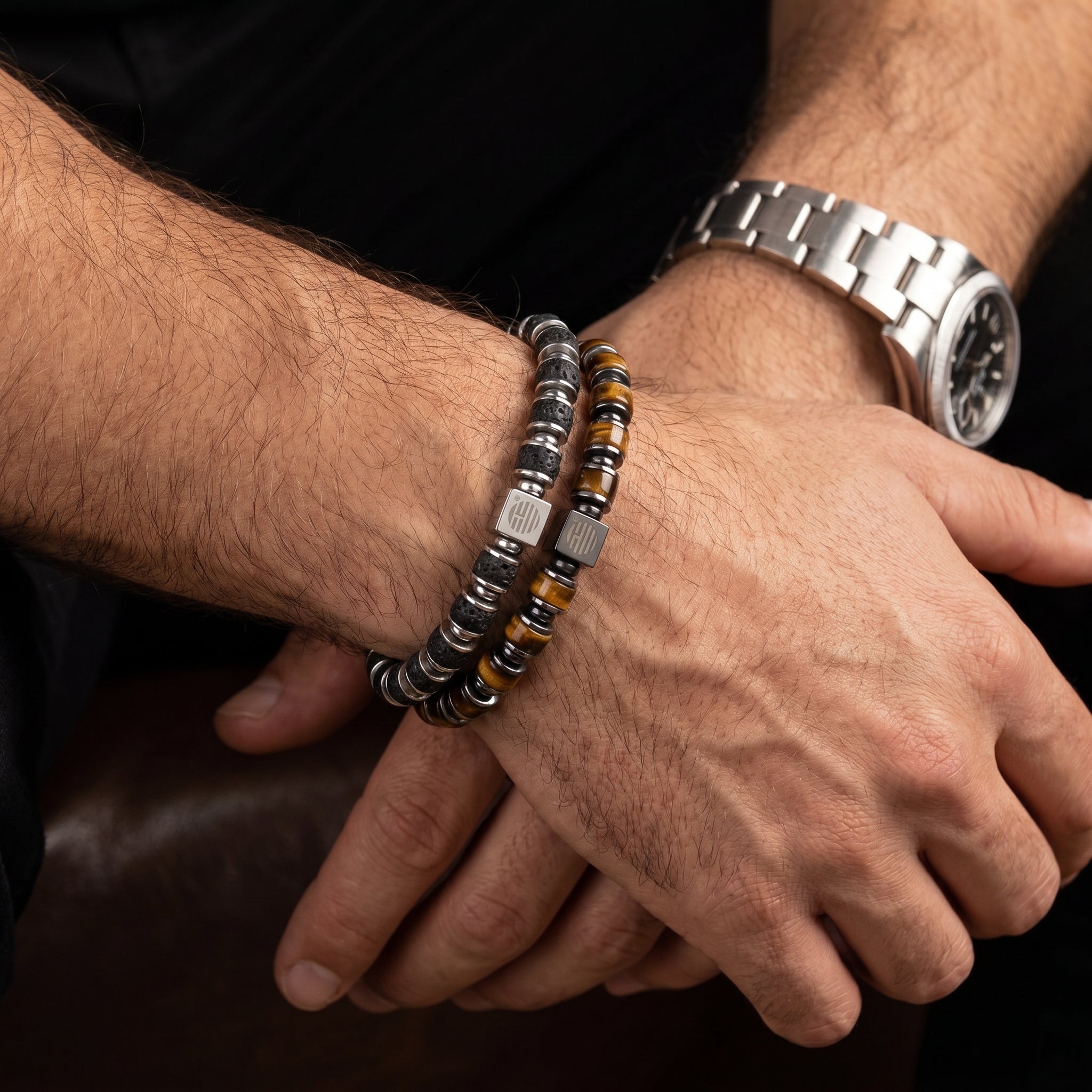 Close-up of a person's wrist wearing a silver watch and beaded bracelets on a dark background