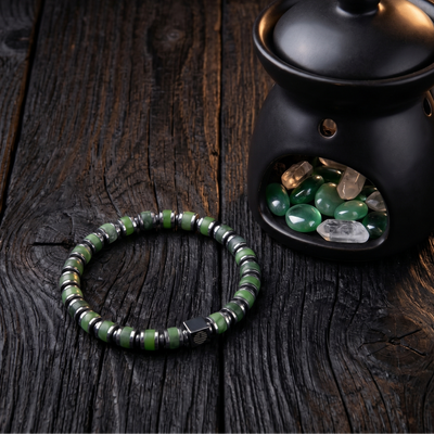 Black ceramic oil burner with green stones on a wooden surface, next to a green beaded bracelet.