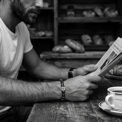 Man wearing my enchanter black obsidian bracelet reading a newspaper in a bakery with bread in the background